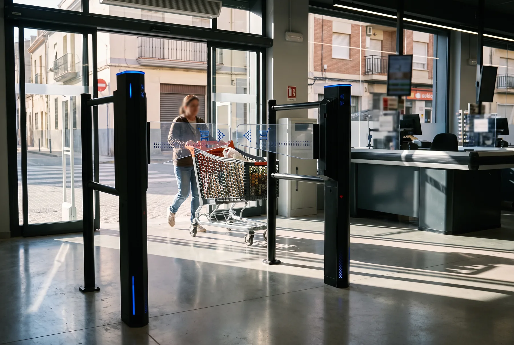 Cliente con carrello che esce da un supermercato attraverso un varco intelligente nero con bracci acrilici LED